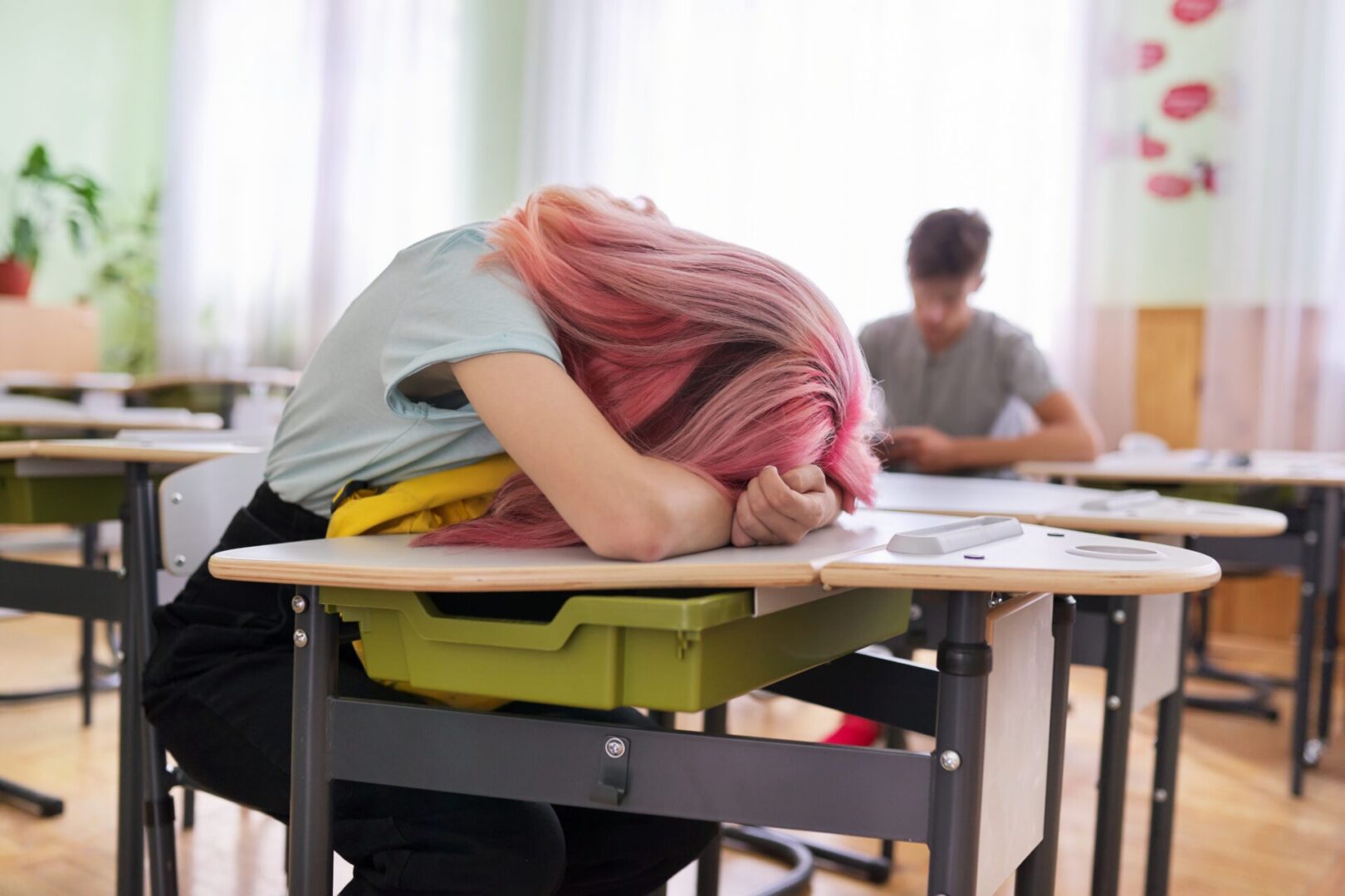 Tired teenage student asleep on her desk. Girl put her head on a backpack, classroom background